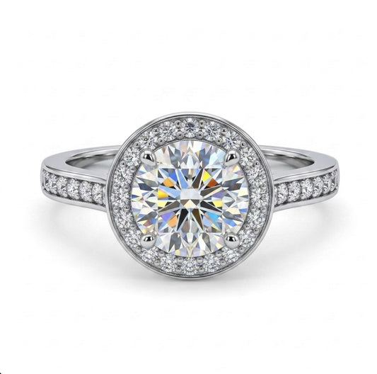A round halo engagement ring featuring a large brilliant-cut center stone surrounded by a double halo of smaller stones, set in a silver-colored metal band with pavé accents on the shoulders, shown on a white background.