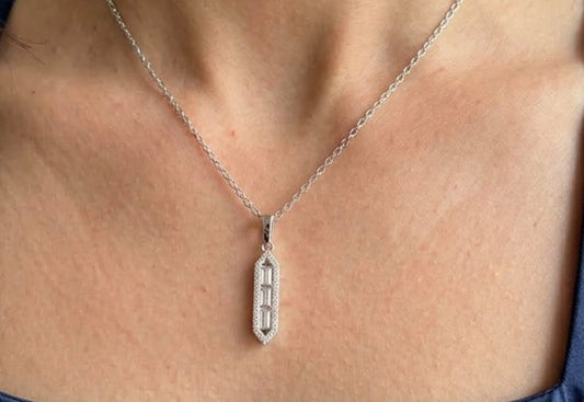 A close-up of a person's neck and chest wearing a delicate silver chain necklace with a vertical rectangular pendant featuring a geometric cutout design.