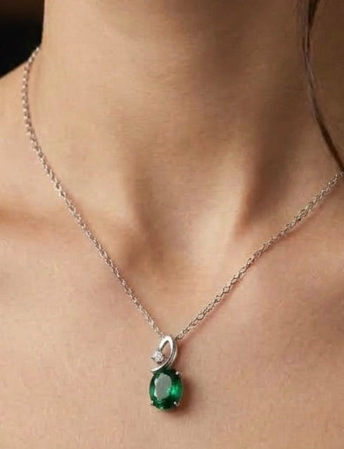 A close-up of a model's neck and chest wearing a delicate silver chain necklace with a pendant featuring a round green gemstone and a small clear accent stone. Make it small the pendent 
